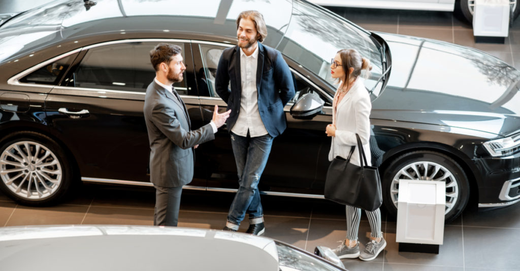 young-couple-with-salesman-in-car-showroom