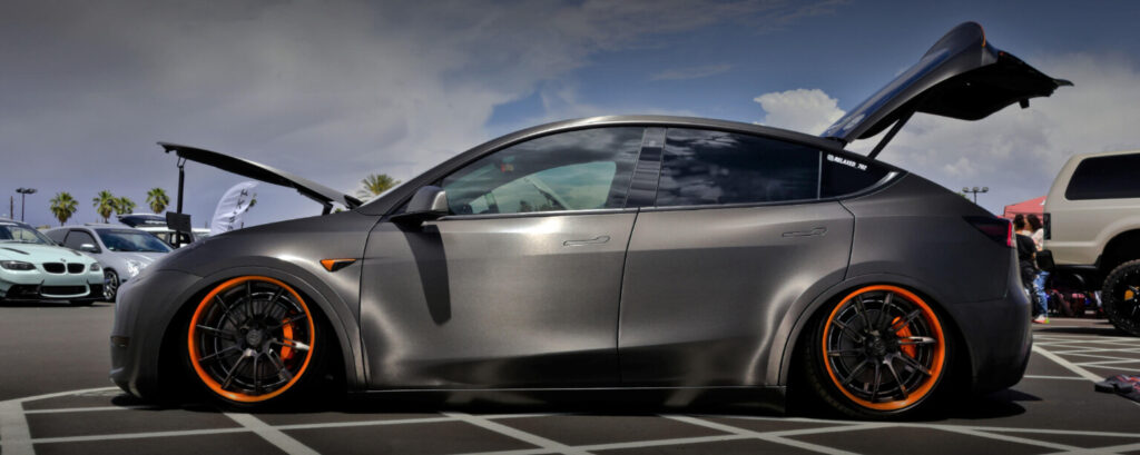 Image showing highly modified Tesla Model X with orange cambered tyre rims and a lowered chassis. 